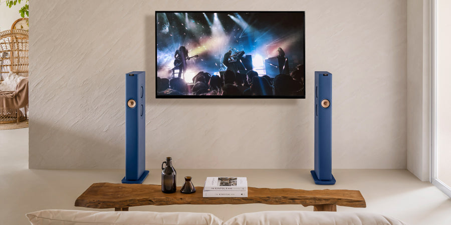 Une paire d'enceintes KEF LS60 Wireless entre une télévision diffusant un concert en direct dans un salon