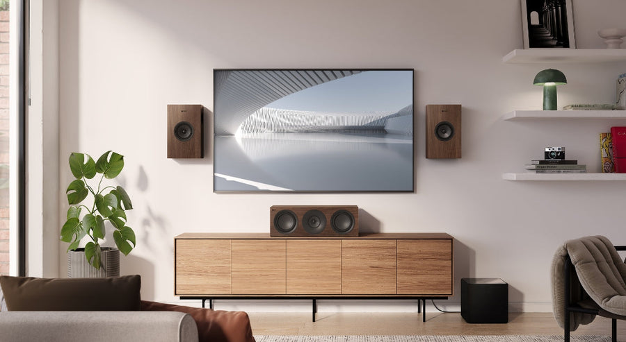 Installation home cinéma élégante avec enceintes KEF Q Series finition noyer, enceinte centrale et caisson de basses, disposés autour d’une télévision murale dans un salon moderne au style scandinave.