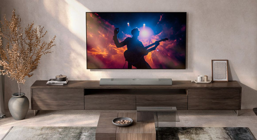 Télévision murale diffusant le silhouette d’un guitariste en concert en direct, au-dessus d’un meuble multimédia moderne en bois avec une barre de son élégante.