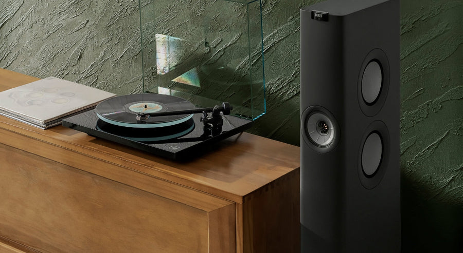 Enceinte HiFi colonne KEF placée à côté d’une platine vinyle sur un meuble audio en bois dans un salon moderne