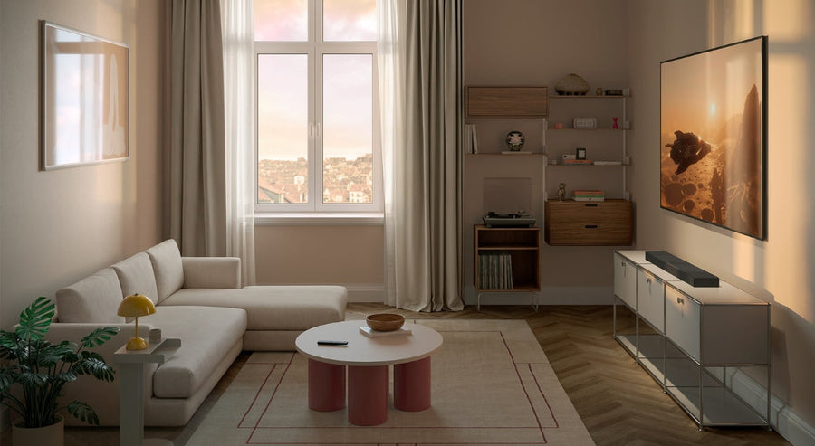 Salon moderne avec téléviseur mural, canapé d’angle beige, lumière naturelle douce et décoration minimaliste dans des tons neutres.